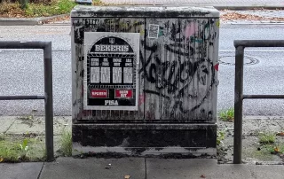 Street view of an electric box wearing a poster of the relief print "Bekersis-education-pokie" by street artist LAPIZ in Hamburg